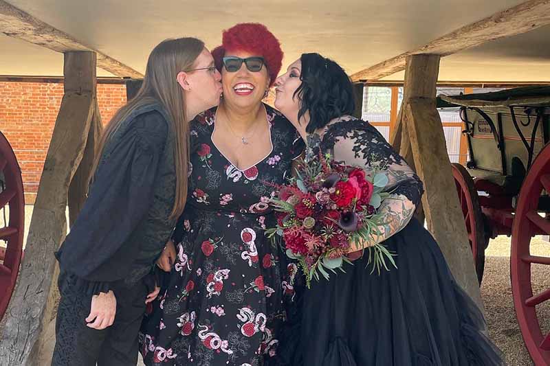 Magical celebrant wedding ceremonies. A bride and groom dressed in black, kissing me on the cheeks as I stand between them grinning  