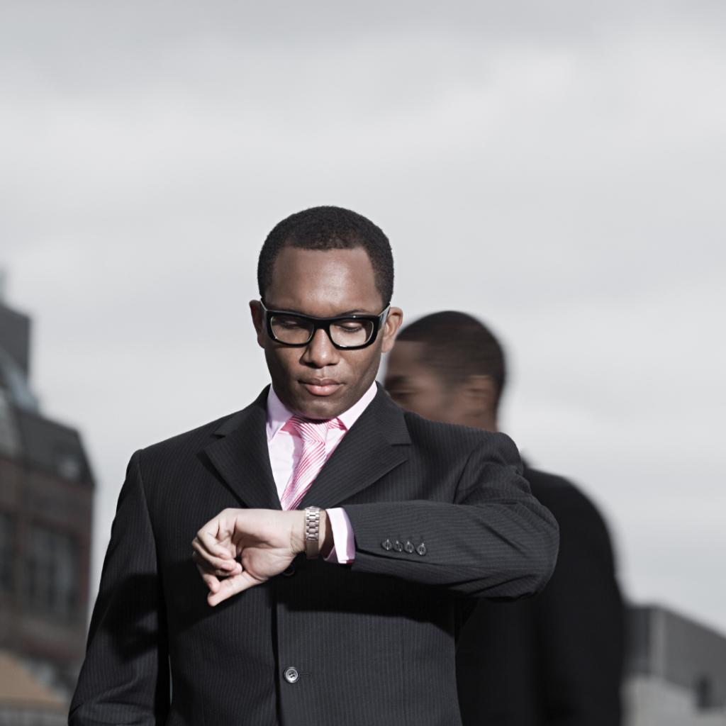 ARRIVE ON TIME BLACK MAN WEARING A SUIT LOOKING AT HIS WRIST WATCH 